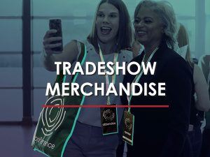 Two women wearing a branded tote bag and branded lanyard while attending a trade show.